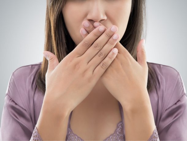 woman with dark hair and both hands covering her mouth