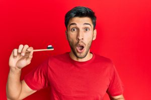 surprised man holding toothbrush about to brush teeth with non vegan toothpaste